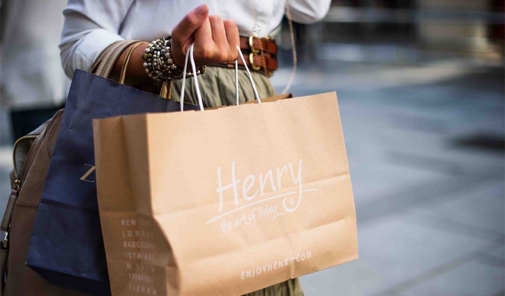 Person holding several shopping bags, including a prominently visible bag with the brand name "Henry" and the website "enjoyhenry.com" printed on it. northern ireland wedding photographer